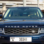 Front view of a navy blue Range Rover with its logo visible, parked in an urban setting under a modern overpass.