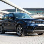 A sleek blue Range Rover Sport parked on a modern paved area with architectural structures in the background.