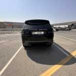 A black Range Rover Sport parked in an empty lot with a clear sky and buildings in the background.