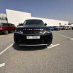 Front view of a black Range Rover in a parking lot, with a red Range Rover nearby and a row of various cars in the background.