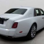 A sleek white Rolls-Royce luxury sedan captured from the rear, showcasing its elegant design and polished alloy wheels.