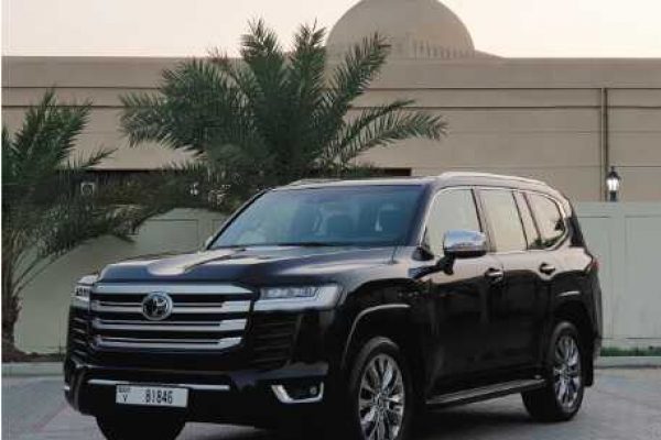 A black SUV Land Cruiser is parked on a paved area, with palm trees and a building featuring a dome and crescent in the background.
